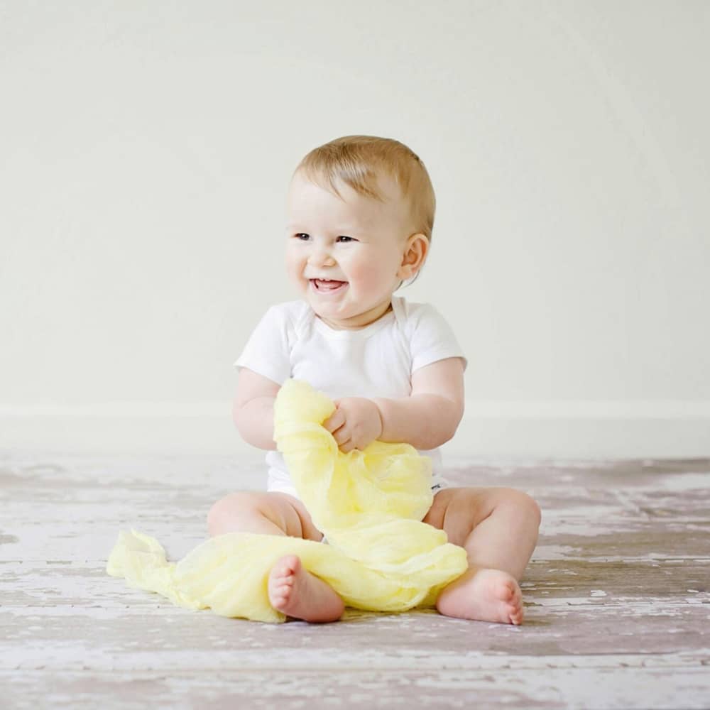 smiling baby holding bright yellow blanket